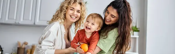 Happy lesbian couple having fun together with their cute baby girl holding tangerines, banner — Stock Photo