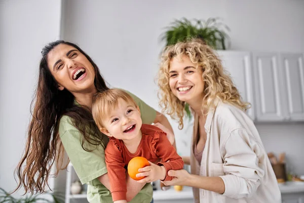 Liebendes lesbisches Paar, das zusammen mit ihrem süßen Baby-Mädchen mit Mandarinen Spaß hat, Familie — Stockfoto