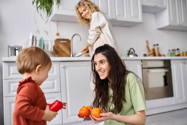 Se concentrer sur la femme heureuse avec sa fille tenant des mandarines avec son partenaire blond flou sur toile de fond — Photo de stock