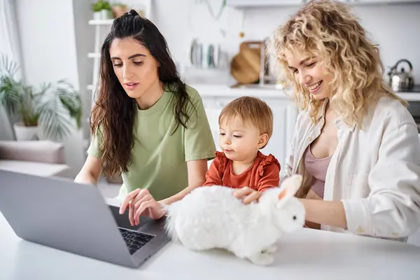 Пов'язана лесбіянка пара в домашньому одязі дивитися фільми зі своєю дитиною на ноутбуці, сімейна концепція — стокове фото