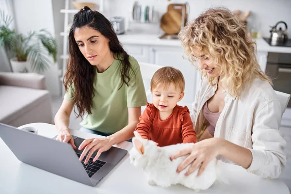 Positive lesbian couple in homewear watching movies with their baby girl on laptop, family concept — Stock Photo
