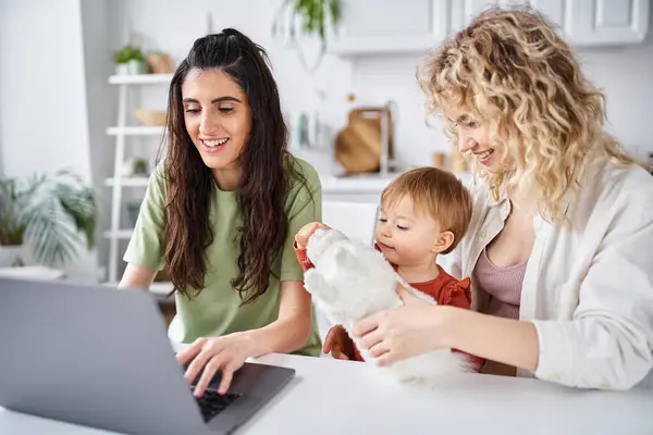 Nutrir pareja lesbiana en ropa de casa viendo películas con su bebé en el ordenador portátil, concepto de familia - foto de stock