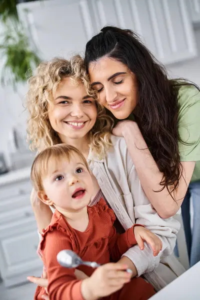 Happy lgbt couple in homewear spending time with their daughter on kitchen, spoons in hand — Stock Photo