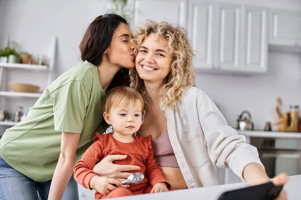 Lustiges lgbt-Paar, das Zeit mit seiner Tochter verbringt, mit Löffeln in der Hand und Telefon in der Hand, Familie — Stockfoto