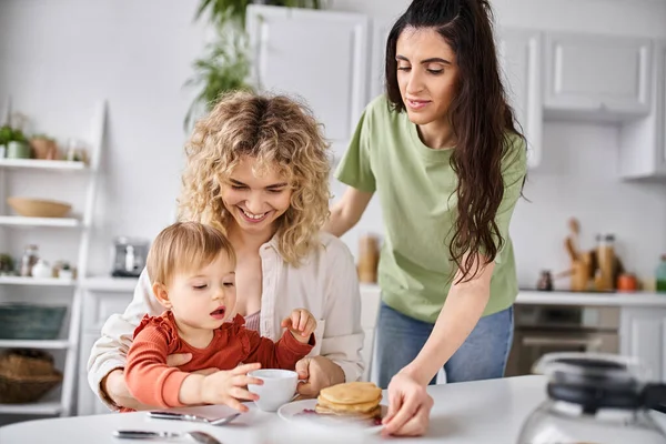 Jolly beautiful lgbt couple in homewear having great time with their daughter at breakfast, family — Stock Photo