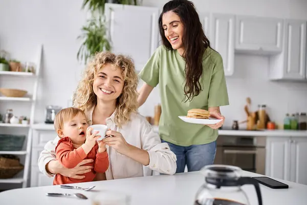 Радостный очаровательный lgbt пара в домашней одежде, отлично провести время со своей дочерью за завтраком, семья — стоковое фото