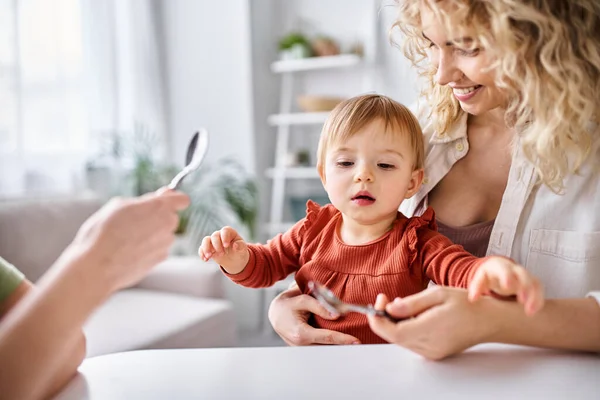 Cute little baby girl surrounded by her attractive mothers that holding spoons, family concept — Stock Photo
