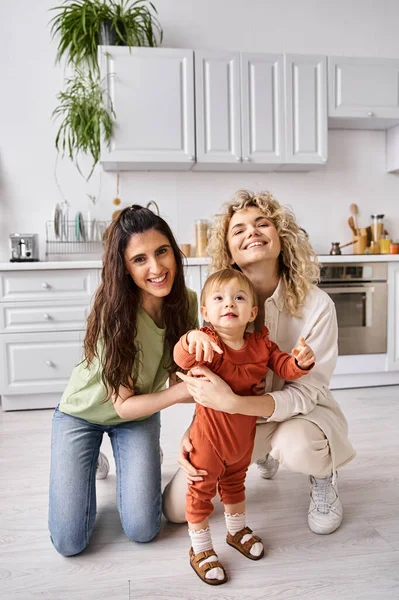 Charming jolly lesbian couple in homewear spending time together with their toddler daughter — Stock Photo