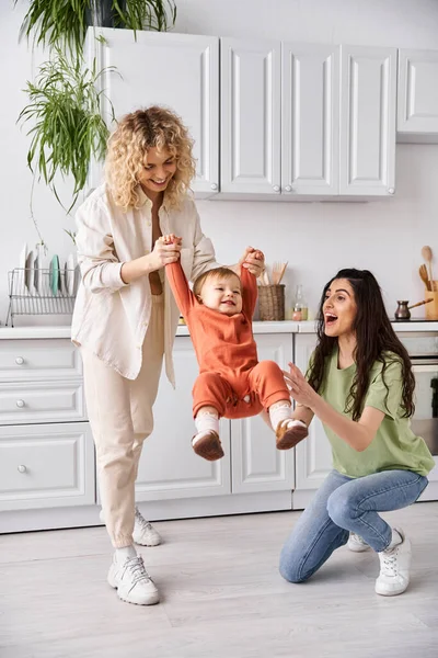 Attractive cheerful lesbian couple playing actively with their toddler daughter, modern parenting — Stock Photo