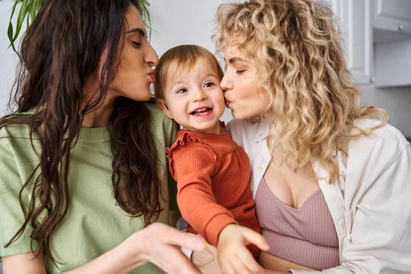 Amante alegre pareja lesbiana en ropa de casa posando felizmente con su bebé niña, crianza moderna - foto de stock
