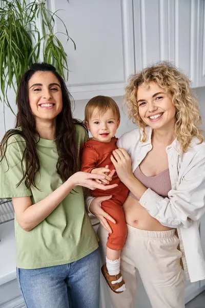 Caring cheerful lesbian couple in homewear posing happily with their baby girl, modern parenting — Stock Photo