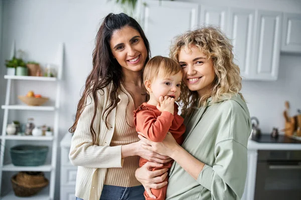 Attraente jolly coppia lesbica in biancheria da casa posa insieme con la loro bambina, concetto di famiglia — Foto stock