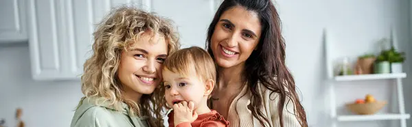 Encantadora pareja lesbiana en ropa de casa posando junto con su bebé, concepto de familia, pancarta - foto de stock