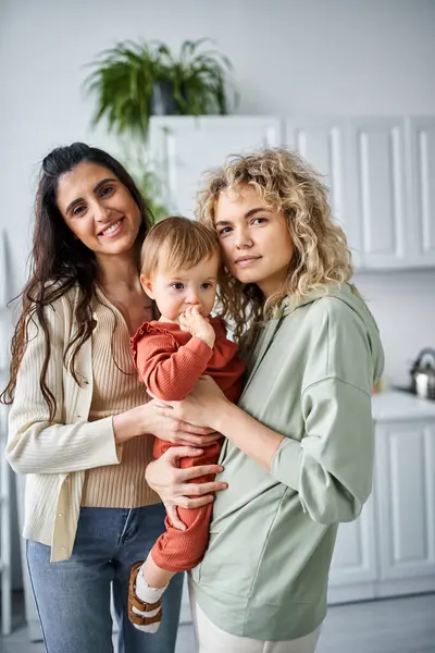 Beau couple lesbien joyeux dans homewear posant avec leur bébé fille, concept de famille — Photo de stock