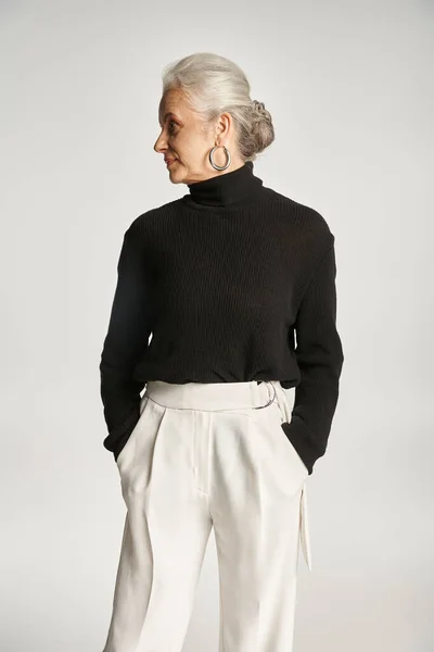 Retrato de mujer de negocios de mediana edad en traje elegante posando con las manos en bolsillos en gris - foto de stock