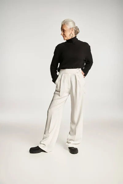 Longitud completa de mujer de negocios de mediana edad en traje elegante posando con las manos en bolsillos en gris - foto de stock