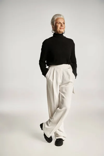 Full length of happy middle aged business woman in elegant attire posing with hands in pockets — Stock Photo