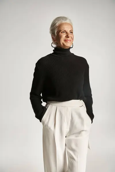 Retrato de mujer de negocios de mediana edad feliz en traje elegante posando con las manos en bolsillos en gris - foto de stock