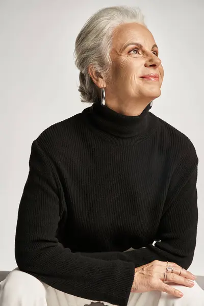 Retrato de negocios, mujer de negocios feliz de mediana edad en cuello alto mirando hacia otro lado en el fondo gris - foto de stock
