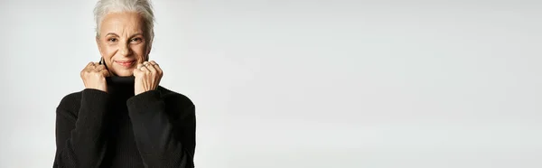 Ritratto di donna d'affari di mezza età che regola il colletto del maglione collo alto su sfondo grigio — Foto stock