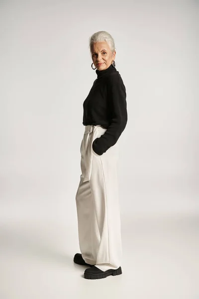 Longitud completa de la mujer de negocios de mediana edad feliz en traje elegante posando con las manos en los bolsillos - foto de stock