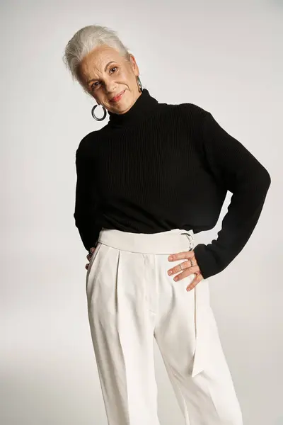 Mujer de negocios de mediana edad feliz en elegante traje casual elegante posando con las manos en las caderas en gris - foto de stock