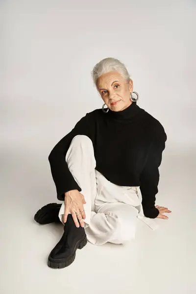 Mujer de negocios feliz de mediana edad en elegante atuendo casual elegante sentado sobre fondo gris - foto de stock