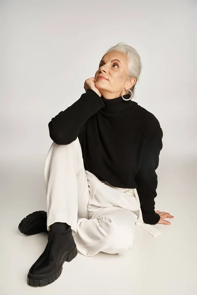 Dreamy middle aged business woman in elegant smart casual attire sitting on grey background — Stock Photo