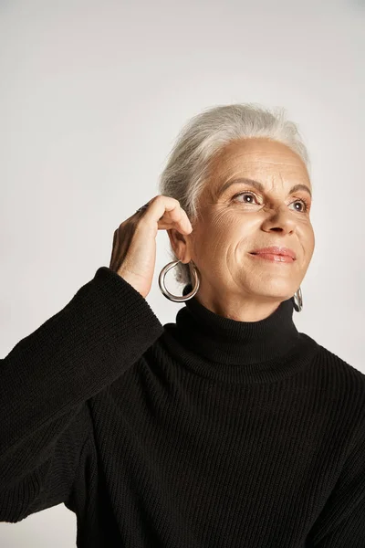 Happy middle aged business woman in elegant attire wearing hoop earrings on grey background — Stock Photo