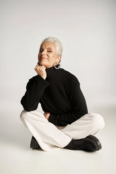 Alegre mujer de negocios de mediana edad en elegante traje casual elegante sentado sobre fondo gris - foto de stock