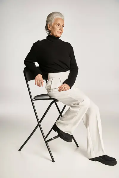 Élégante femme d'affaires d'âge moyen en tenue décontractée intelligente et boucles d'oreilles cerceau assis sur chaise sur gris — Photo de stock