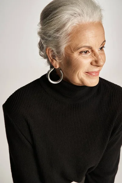 Retrato de mujer de negocios alegre de mediana edad en traje elegante y pendientes de aro sobre fondo gris - foto de stock