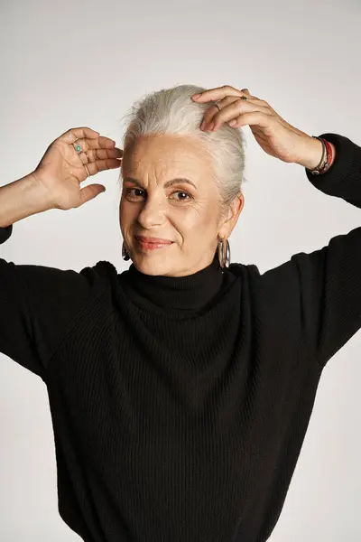 Portrait of happy middle aged business woman in elegant attire and hoop earrings adjusting grey hair — Stock Photo