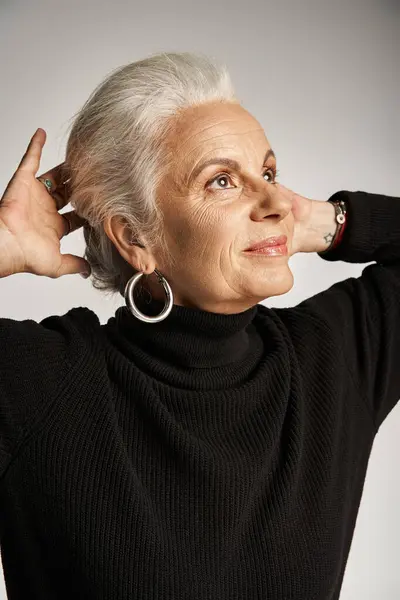 Portrait of happy middle aged business woman in elegant attire and hoop earrings adjusting grey hair — Stock Photo