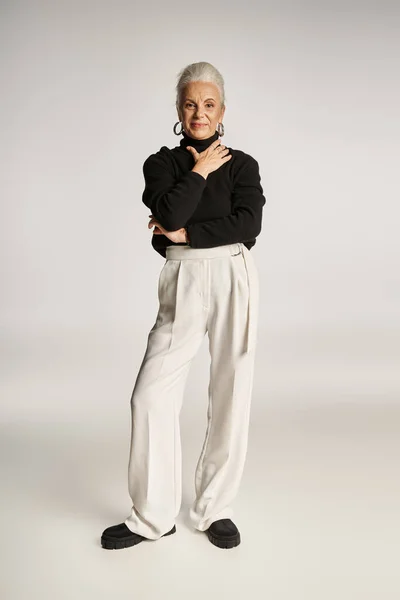 Happy middle aged business woman in elegant attire and hoop earrings standing on grey backdrop — Stock Photo