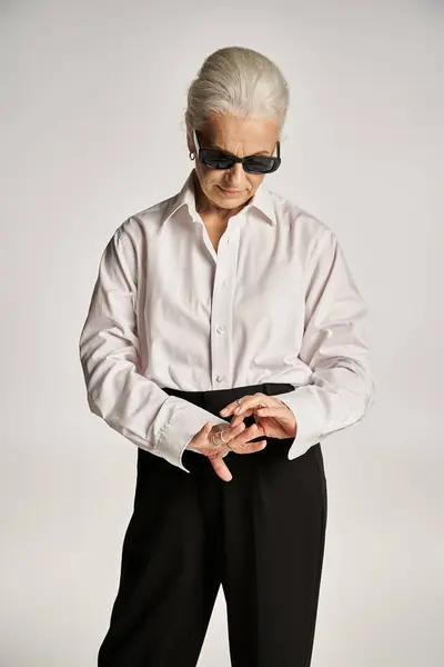 Stylish middle aged woman in white shirt, black pants and sunglasses looking at rings on fingers — Stock Photo