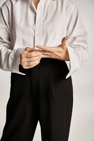 Cropped middle aged woman in white shirt, black pants touching rings on fingers on grey backdrop — Stock Photo