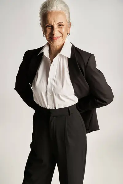 Ritratto di allegra donna d'affari di mezza età in camicia bianca e pantaloni in piedi su sfondo grigio — Foto stock