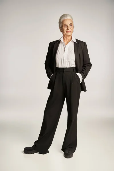 Piena lunghezza di felice donna d'affari di mezza età in camicia e pantaloni in piedi con le mani in tasca — Foto stock