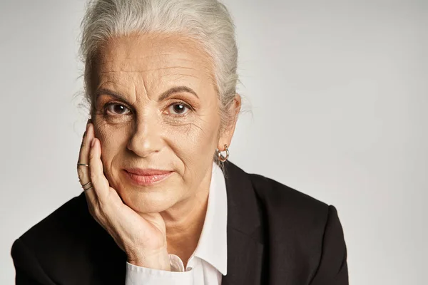 Beautiful and grey haired middle aged woman in elegant attire posing on grey background — Stock Photo