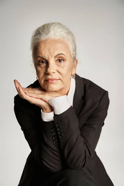 Beautiful and grey haired middle aged woman in elegant attire posing on grey background — Stock Photo