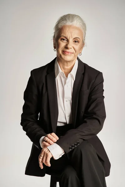 Beautiful and grey haired middle aged woman in elegant attire posing on grey background — Stock Photo