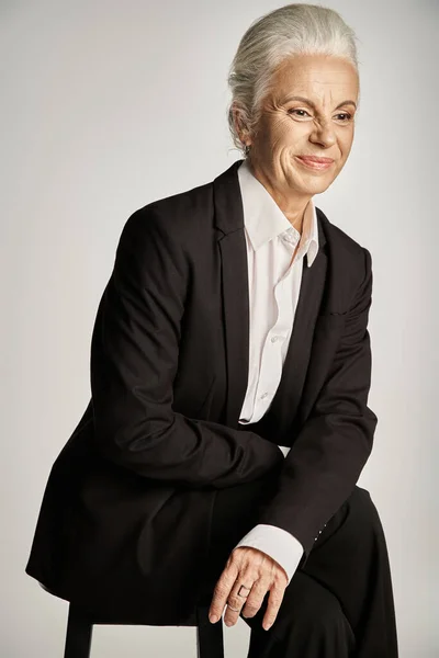 Beautiful and grey haired middle aged woman in elegant attire posing on grey background — Stock Photo
