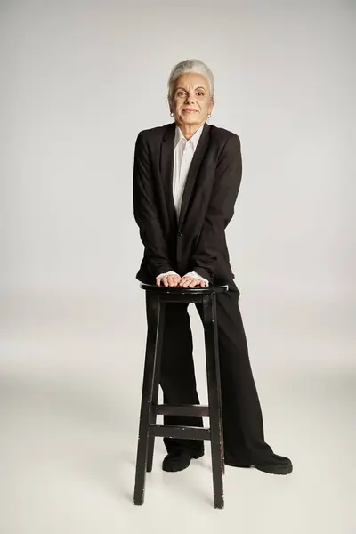 Beautiful and grey haired middle aged woman in elegant attire posing on grey background — Stock Photo
