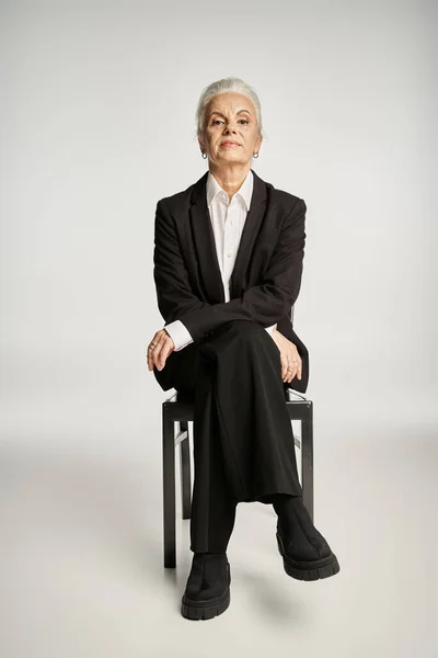 Beautiful and grey haired middle aged woman in elegant attire posing on grey background — Stock Photo