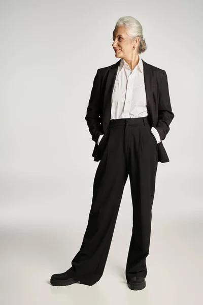 Beautiful and grey haired middle aged woman in elegant attire posing on grey background — Stock Photo