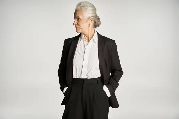 Beautiful and grey haired middle aged woman in elegant attire posing on grey background — Stock Photo