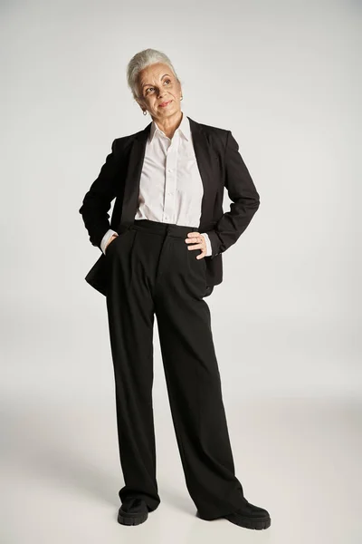 Bella e dai capelli grigi donna di mezza età in elegante abbigliamento in posa su sfondo grigio — Foto stock