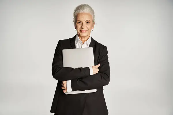 Beautiful and grey haired middle aged woman in elegant attire posing on grey background — Stock Photo