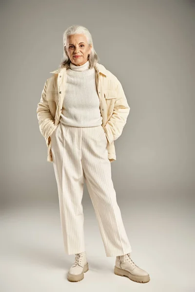 Bella e dai capelli grigi donna di mezza età in elegante abbigliamento in posa su sfondo grigio — Foto stock